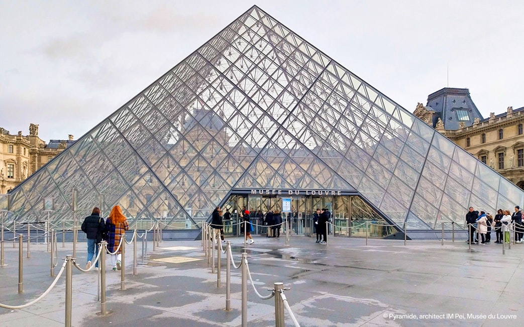 Tourists entering the Louvre Museum through the glass pyramid entrance in Paris.