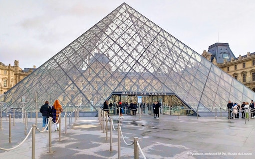 Tourists entering the Louvre Museum through the glass pyramid entrance in Paris.