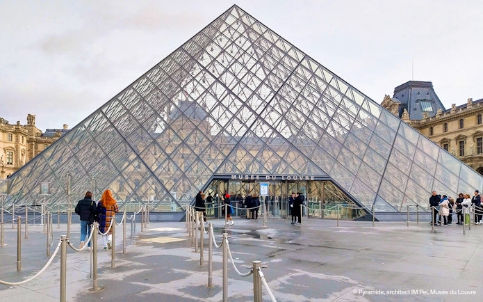 Tourists entering the Louvre Museum through the glass pyramid entrance in Paris.