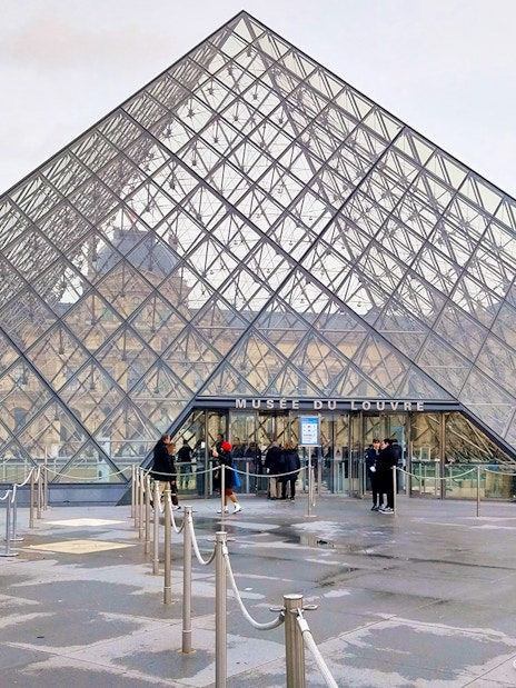 Tourists entering the Louvre Museum through the glass pyramid entrance in Paris.