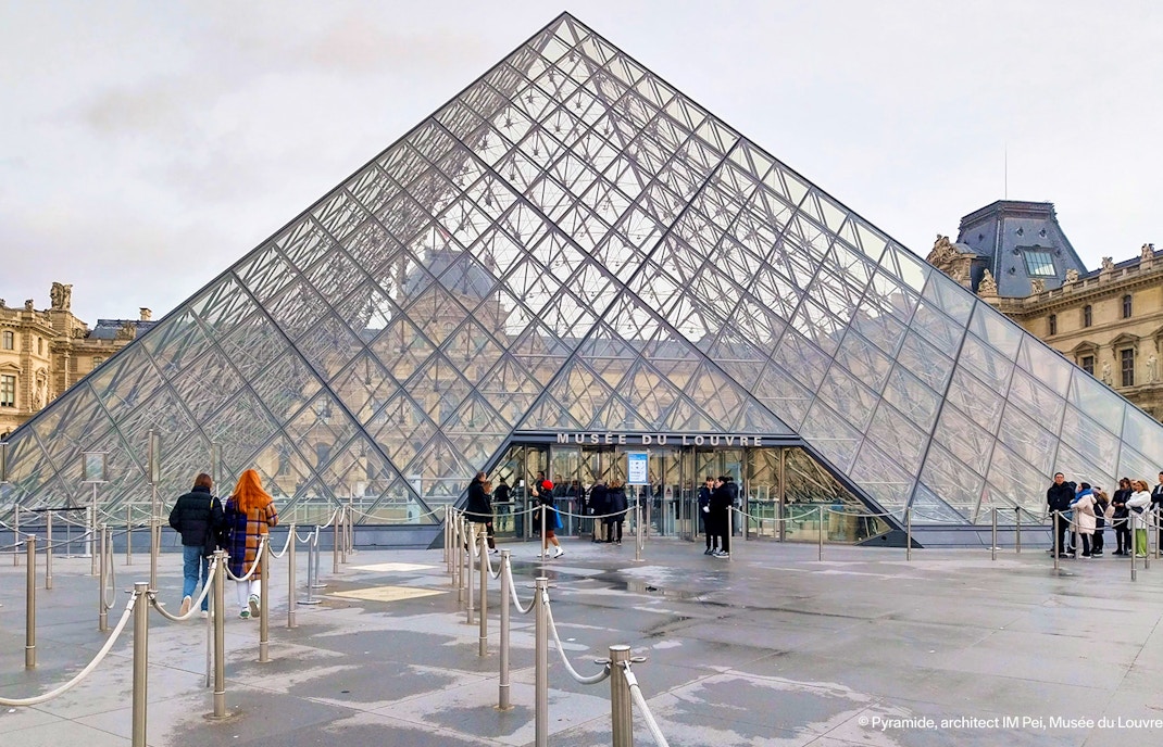Tourist entering Louvre Museum through glass pyramid entrance in Paris, France.