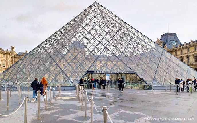 Tourists entering the Louvre Museum through the glass pyramid entrance in Paris.