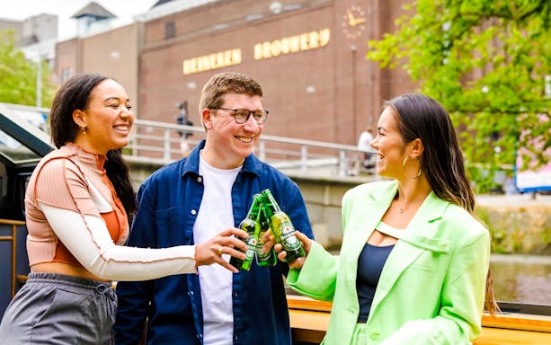 Tourists enjoying Heineken Experience flagship cruise on Amsterdam canal with cityscape views.