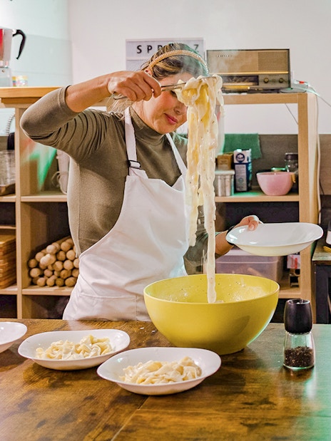 Person preparing pasta in a cooking class kitchen with bowls and ingredients.
