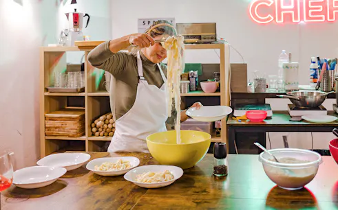 Person preparing pasta in a cooking class kitchen with bowls and ingredients.