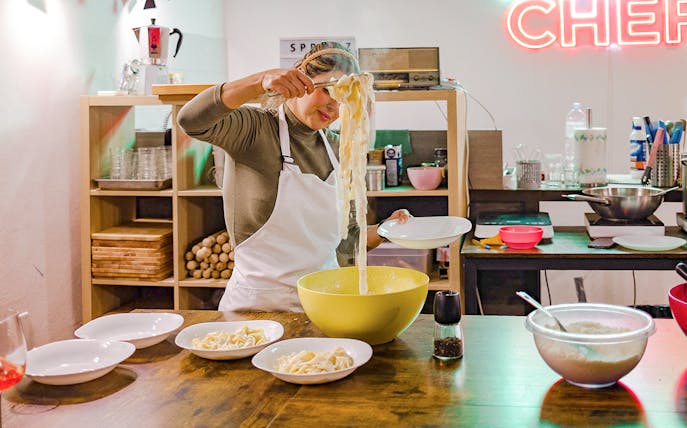 Person preparing pasta in a cooking class kitchen with bowls and ingredients.
