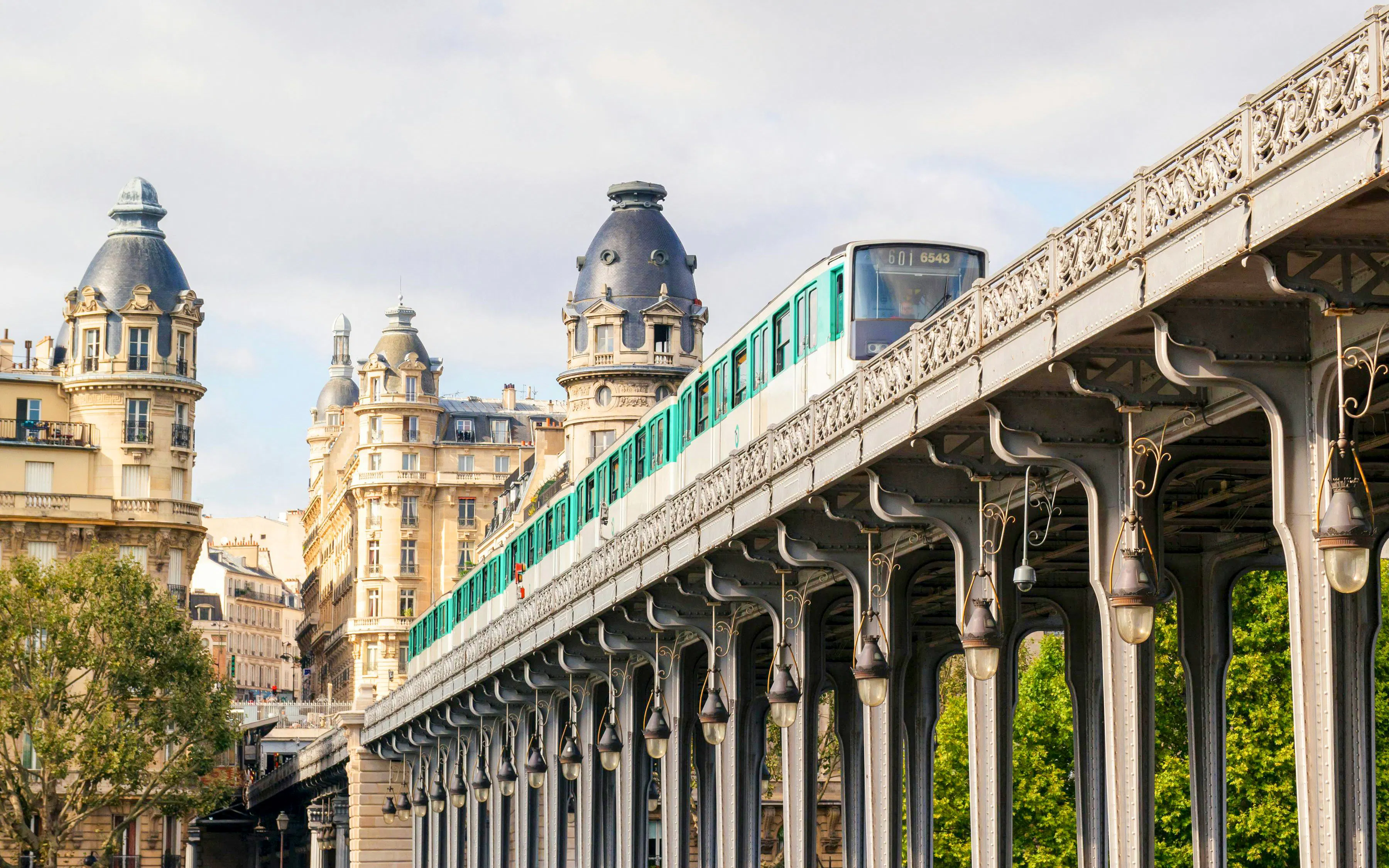 Metro train on elevated tracks between buildings in Paris cityscape, summer.