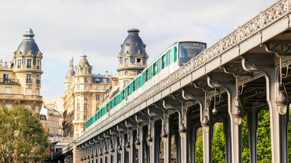 Metro train on elevated tracks between buildings in Paris cityscape, summer.