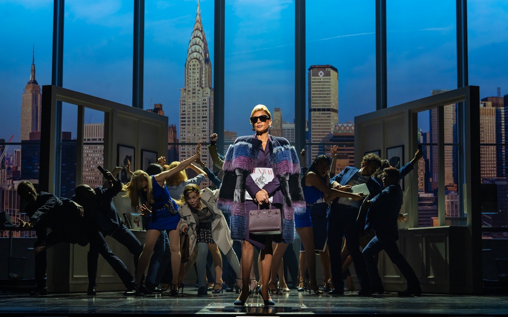 Stage scene from The Devil Wears Prada West End show with city skyline backdrop.