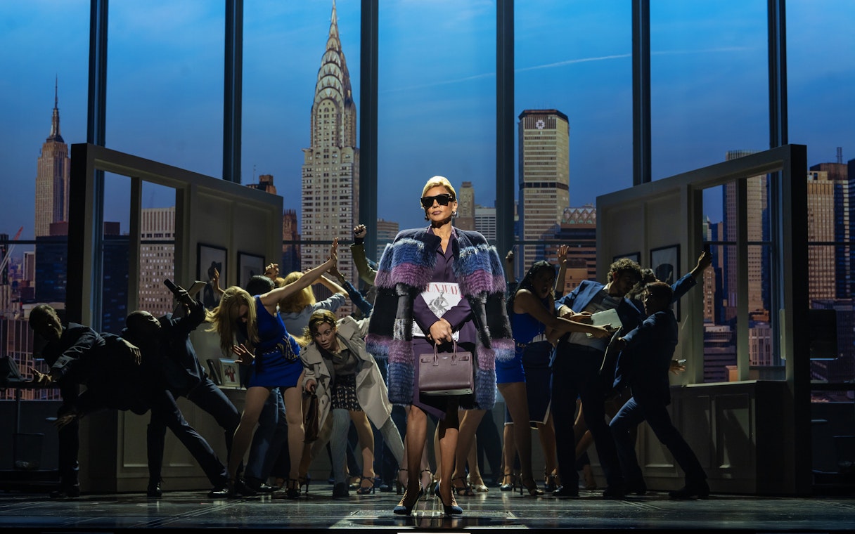 Stage scene from The Devil Wears Prada West End show with city skyline backdrop.