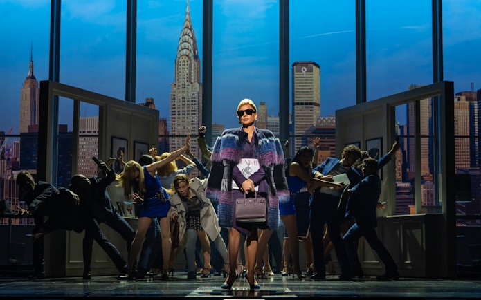 Stage scene from The Devil Wears Prada West End show with city skyline backdrop.
