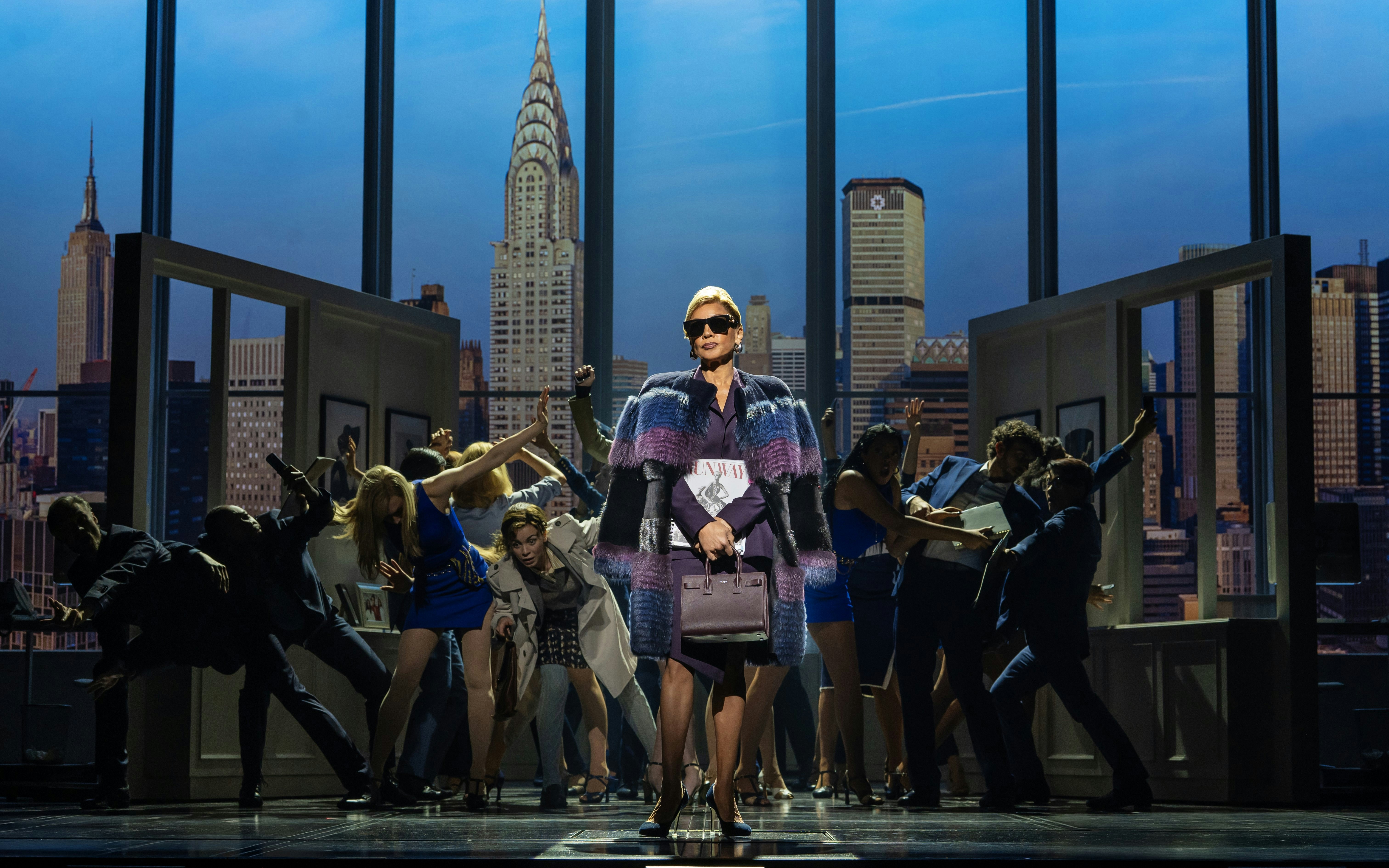 Stage scene from The Devil Wears Prada West End show with city skyline backdrop.