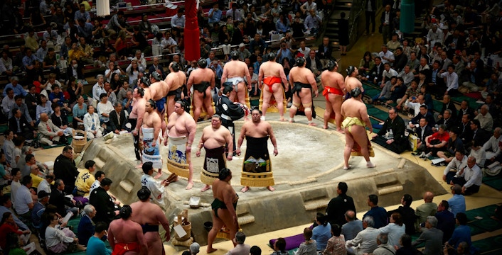 Sumo wrestlers prepare for a match in a crowded Japanese arena.
