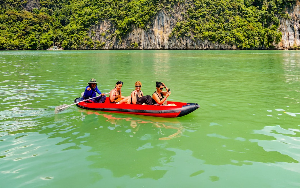 Tourists kayaking in Phang Nga Bay with limestone cliffs in the background.