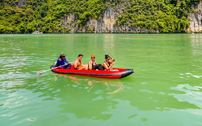 Tourists kayaking in Phang Nga Bay with limestone cliffs in the background.