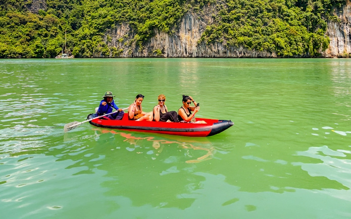 Tourists kayaking in Phang Nga Bay with limestone cliffs in the background.