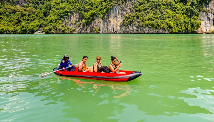 Tourists kayaking in Phang Nga Bay with limestone cliffs in the background.
