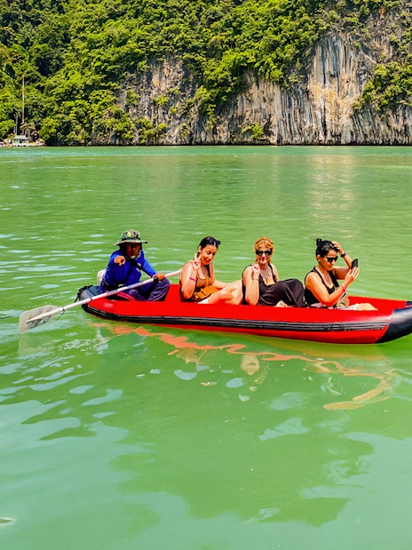 Tourists kayaking in Phang Nga Bay with limestone cliffs in the background.
