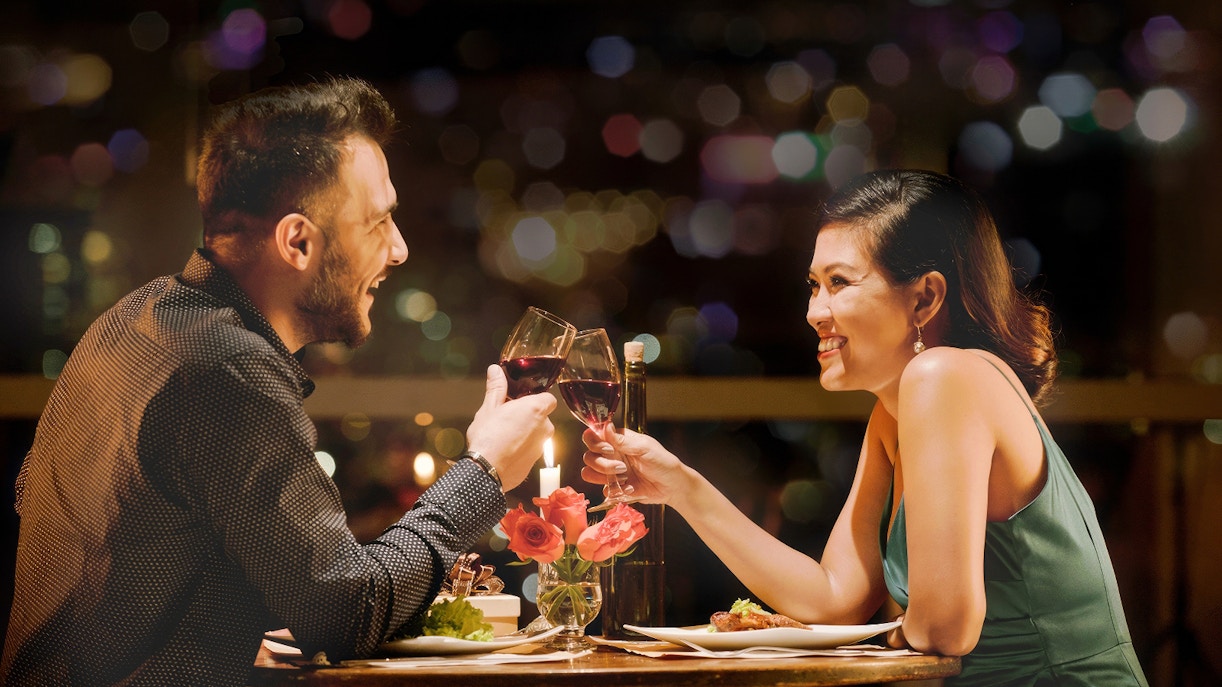 Couple toasting wine glasses on a romantic dinner cruise in Paris.