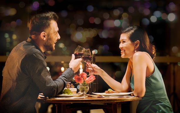 Couple toasting wine glasses on a romantic dinner cruise in Paris.