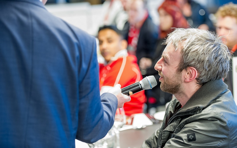 Man speaking into a microphone during Liverpool FC Stadium tour event.