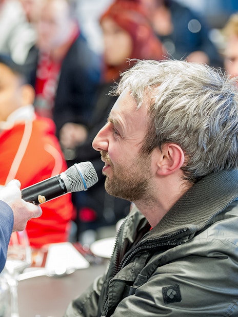 Man speaking into a microphone during Liverpool FC Stadium tour event.
