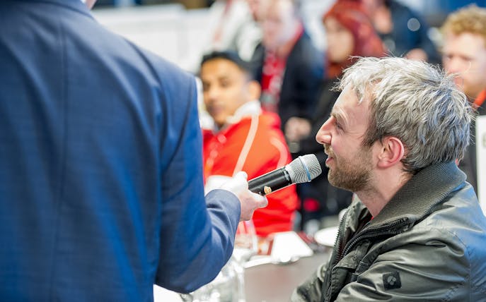 Man speaking into a microphone during Liverpool FC Stadium tour event.