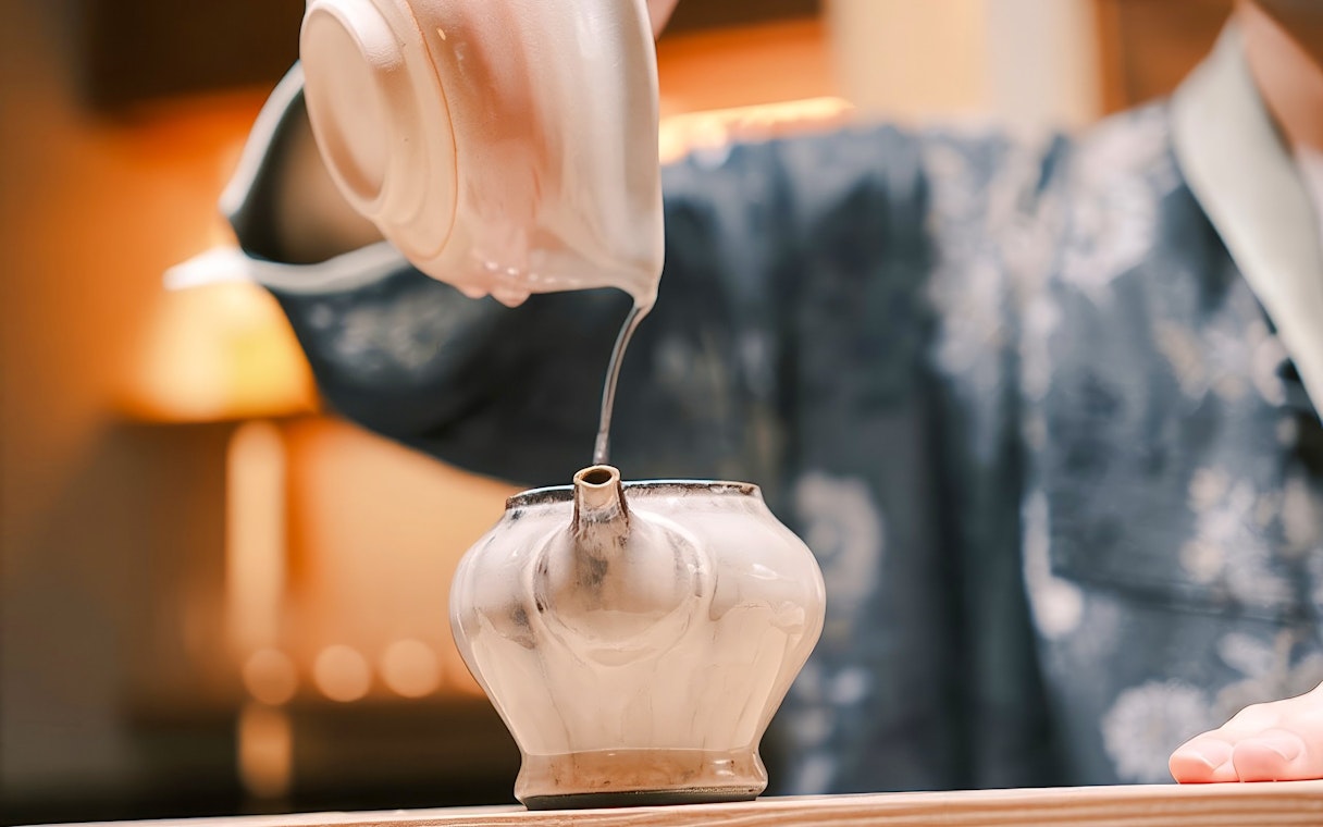 Pouring hot tea into a teapot during a private tea ceremony with seasonal wagashi.