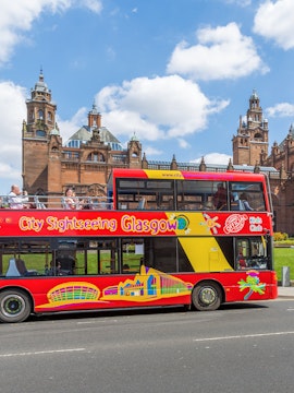 Red double-decker bus for City Sightseeing Glasgow in front of historic building.