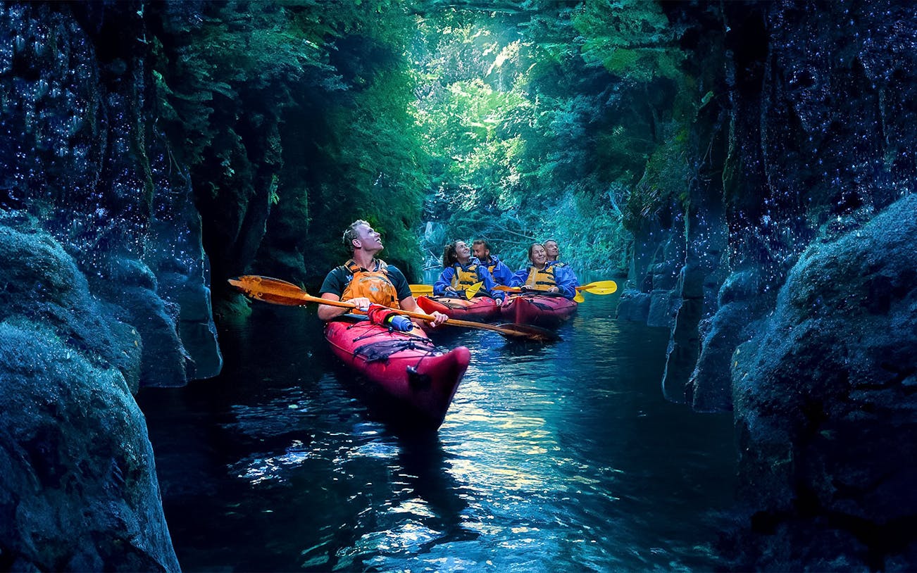 Kayakers explore glowworm-lit cave on evening tour in Tauranga.