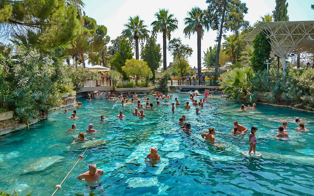 Guests enjoying Cleopatra's Antique Pool in Pamukkale, surrounded by lush greenery.