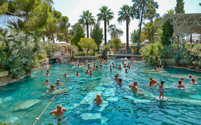 Guests enjoying Cleopatra's Antique Pool in Pamukkale, surrounded by lush greenery.