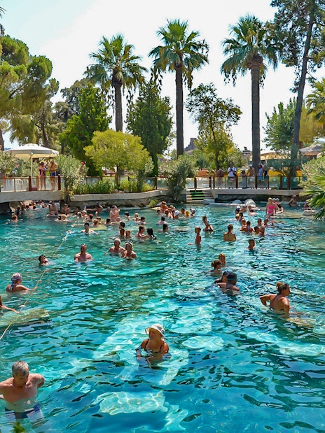 Guests enjoying Cleopatra's Antique Pool in Pamukkale, surrounded by lush greenery.