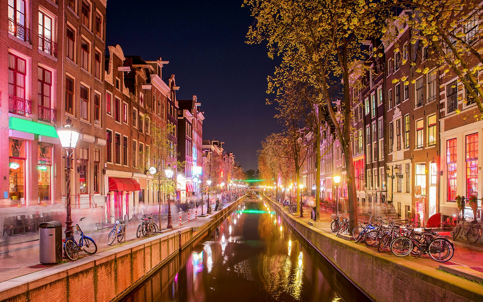 Amsterdam Red Light District canal at night with illuminated buildings and bicycles.