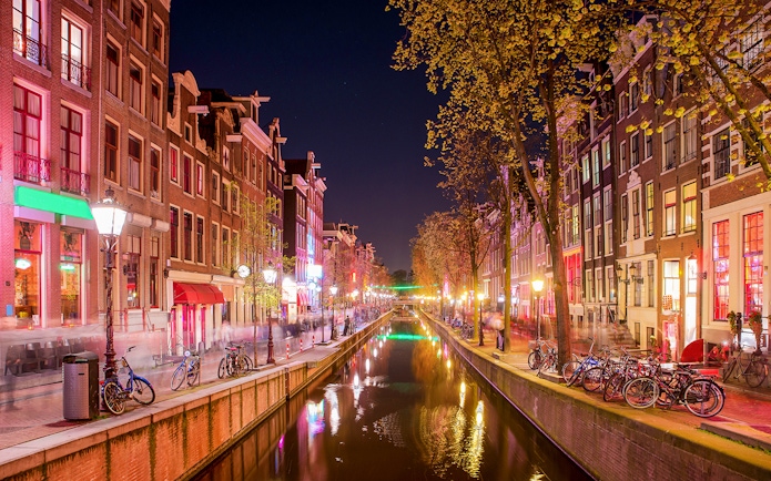 Amsterdam Red Light District canal at night with illuminated buildings and bicycles.