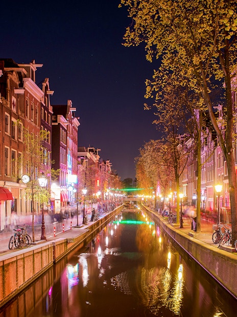 Amsterdam Red Light District canal at night with illuminated buildings and bicycles.