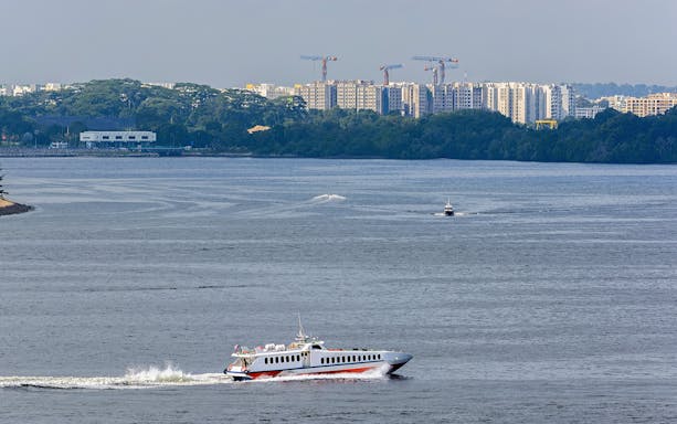 Ferry crossing water with cityscape in background, Harmoni One Batam 2 Days and 1 Night Package.