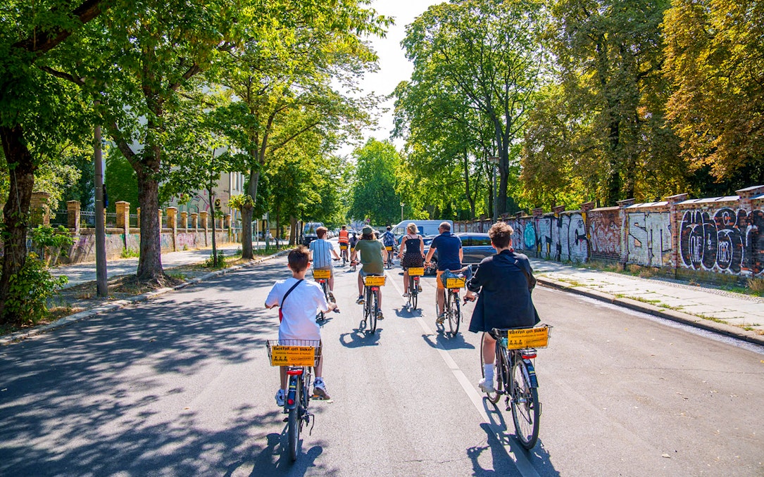 Group biking along graffiti-covered street in Berlin on guided tour.