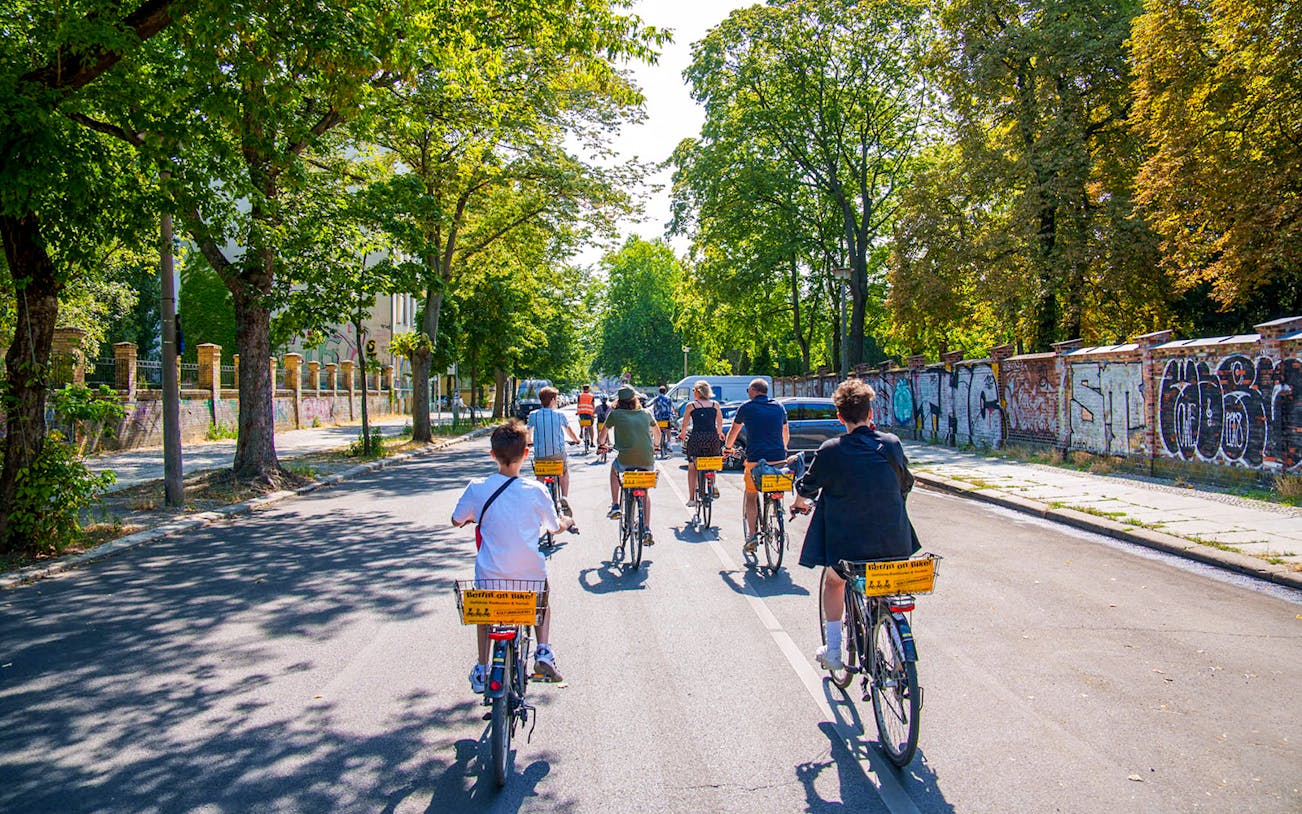 Group biking along graffiti-covered street in Berlin on guided tour.