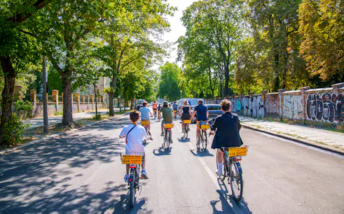 Group biking along graffiti-covered street in Berlin on guided tour.