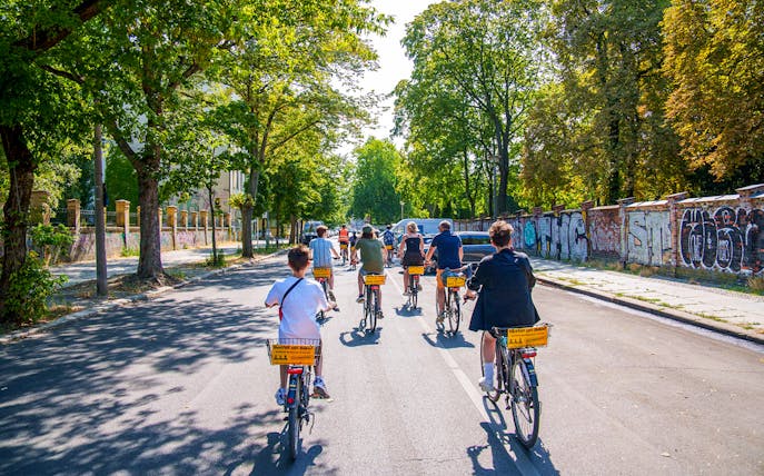 Group biking along graffiti-covered street in Berlin on guided tour.
