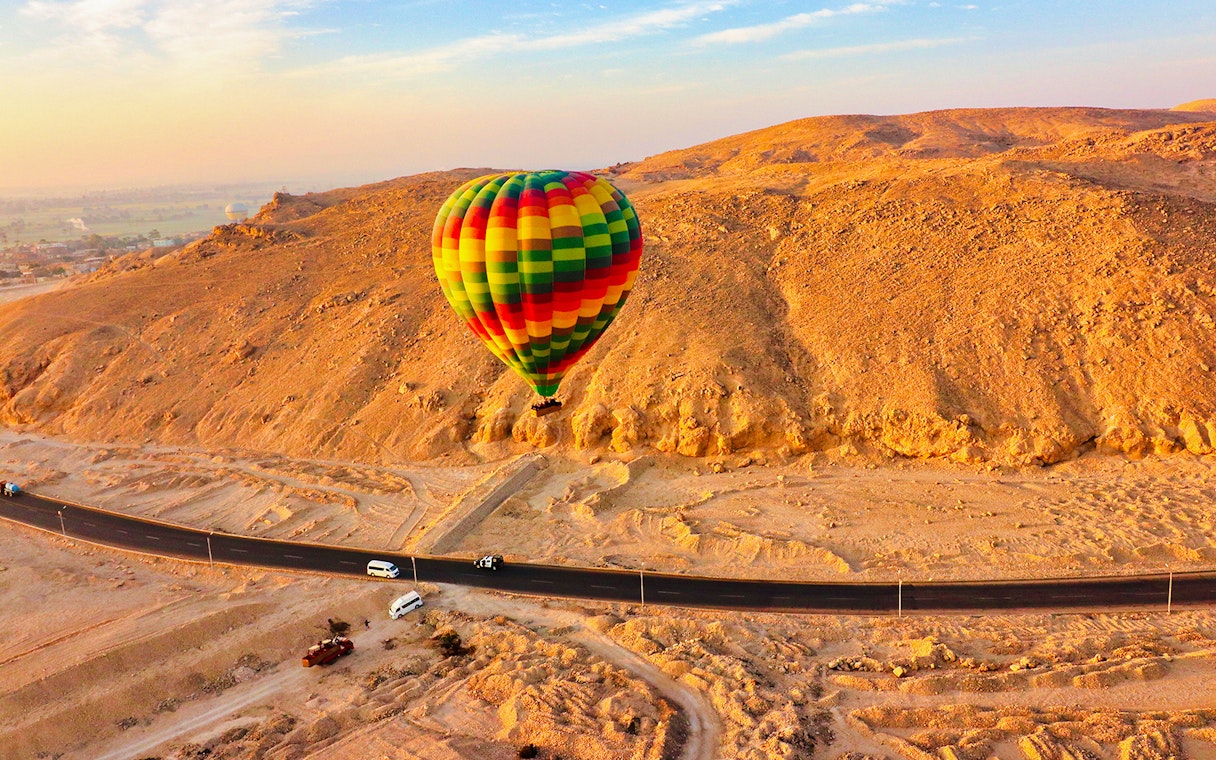 Colorful hot air balloon floating over desert landscape near a road in Egypt.