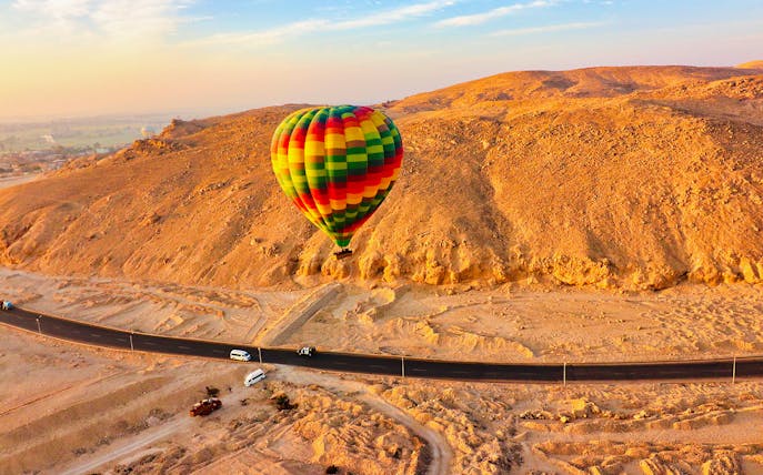 Colorful hot air balloon floating over desert landscape near a road in Egypt.