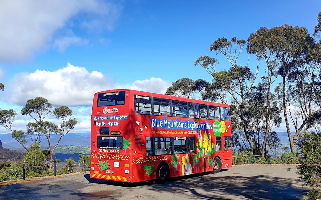 Red double-decker bus on Blue Mountains Hop-On-Hop-Off Tour with scenic view.