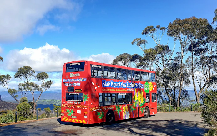 Red double-decker bus on Blue Mountains Hop-On-Hop-Off Tour with scenic view.