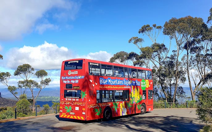 Red double-decker bus on Blue Mountains Hop-On-Hop-Off Tour with scenic view.
