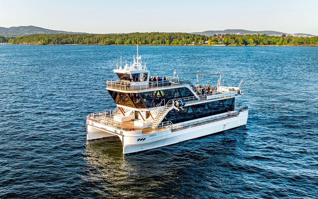Dinner cruise boat on Oslofjord, Norway, with scenic forested shoreline in the background.
