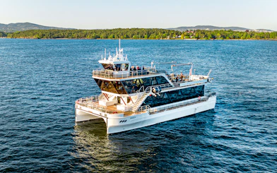 Dinner cruise boat on Oslofjord, Norway, with scenic forested shoreline in the background.