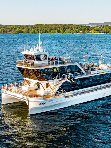 Dinner cruise boat on Oslofjord, Norway, with scenic forested shoreline in the background.