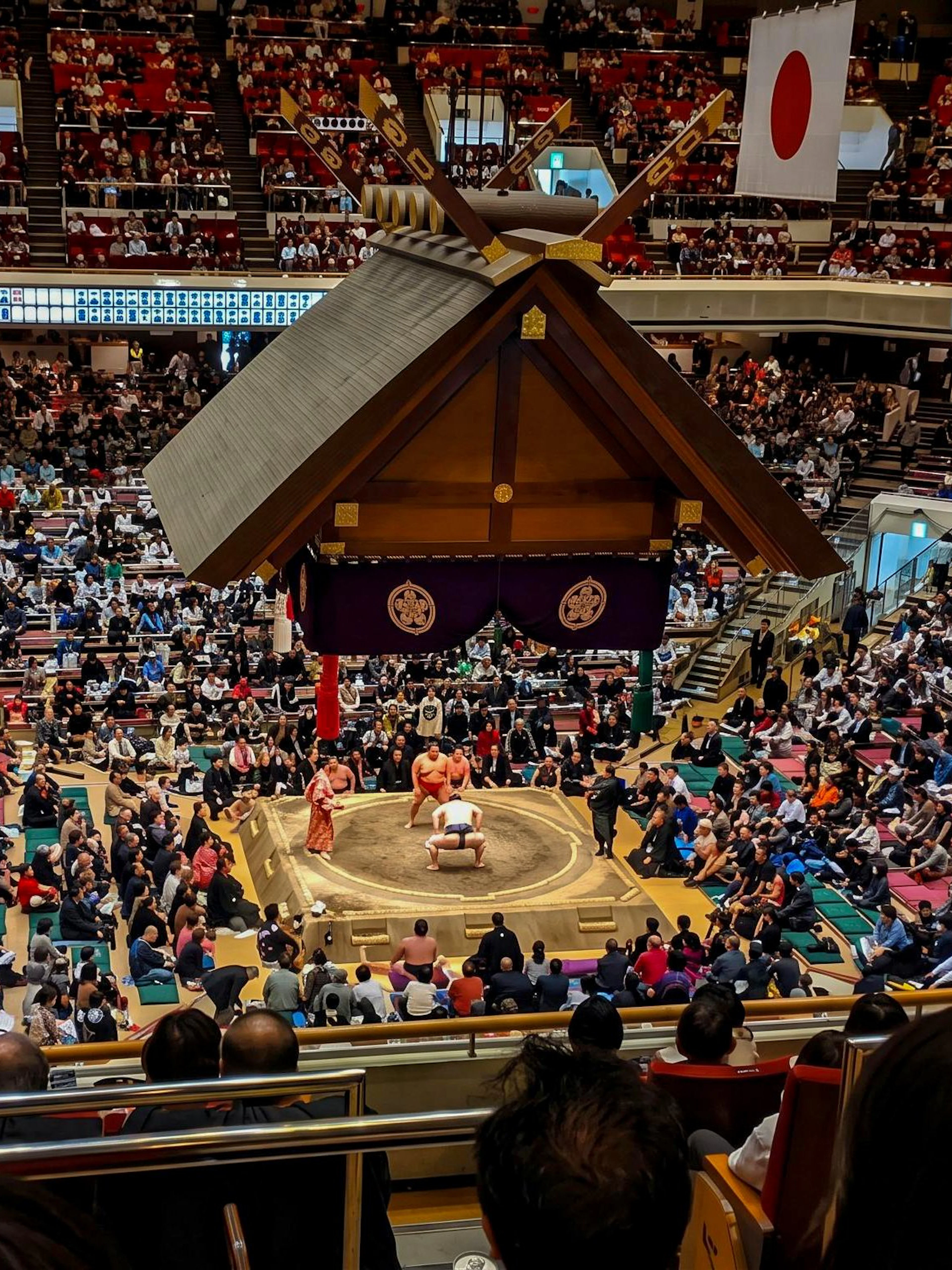 Crowded arena in Tokyo during a Grand Sumo Tournament with spectators watching a match.